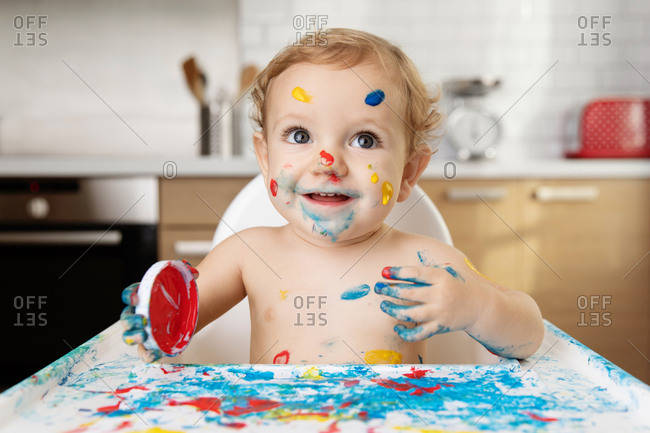Smiling baby in high chair with finger paint on face and body