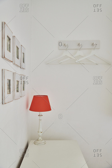 Lamp with red lampshade on a white dresser in a white room
