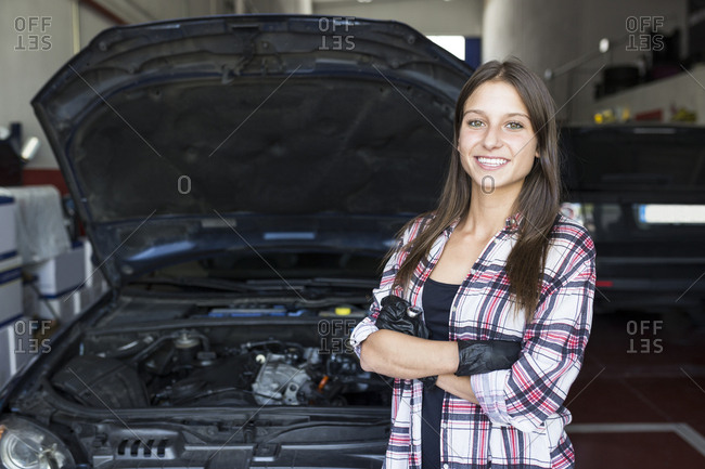 Casual woman in checkered shirt and gloves holding arms crossed and smiling at camera- working in car service