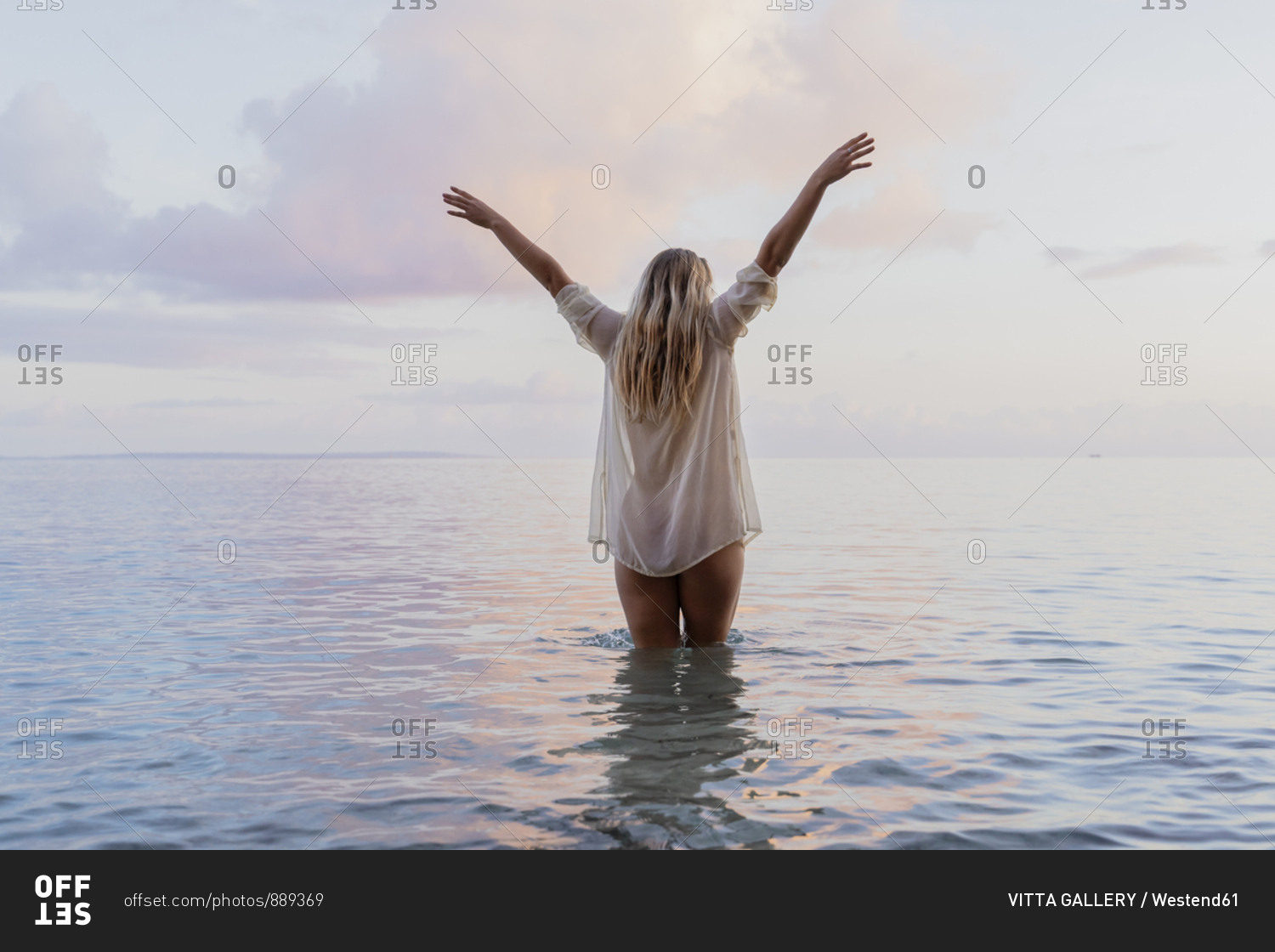 Rear view of young woman wearing white blouse inside sea during sunset