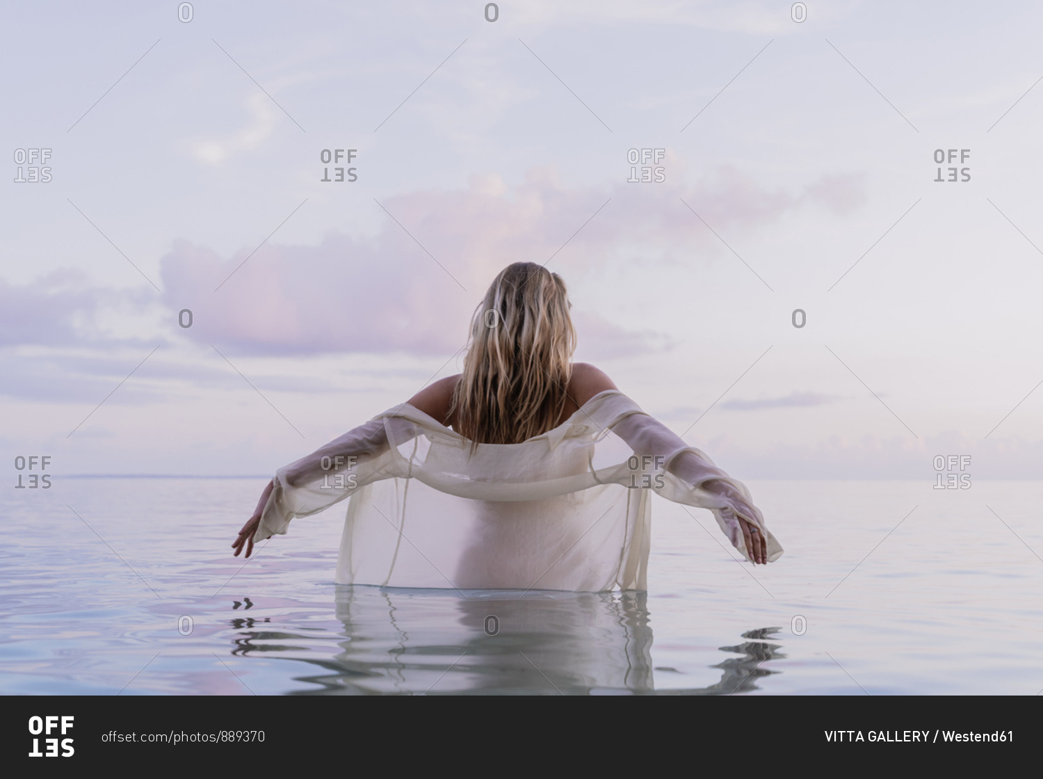 Rear view of young woman wearing white blouse inside sea during sunset