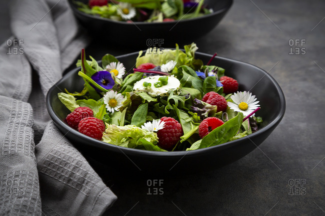 Bowl of fresh salad with arugula- spinach- chard- oak leaf- lollo rosso lettuce- corn salad- raspberries- cream cheese- chive and edible flowers