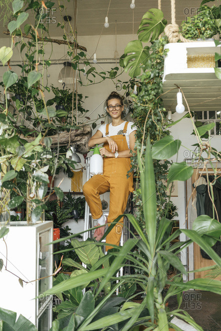 Portrait of a young woman standing on a ladder in a small gardening shop