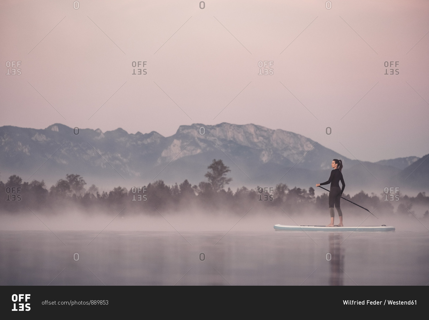 Woman stand up paddling on lake Kirchsee at morning mist- Bad Toelz- Bavaria- Germany
