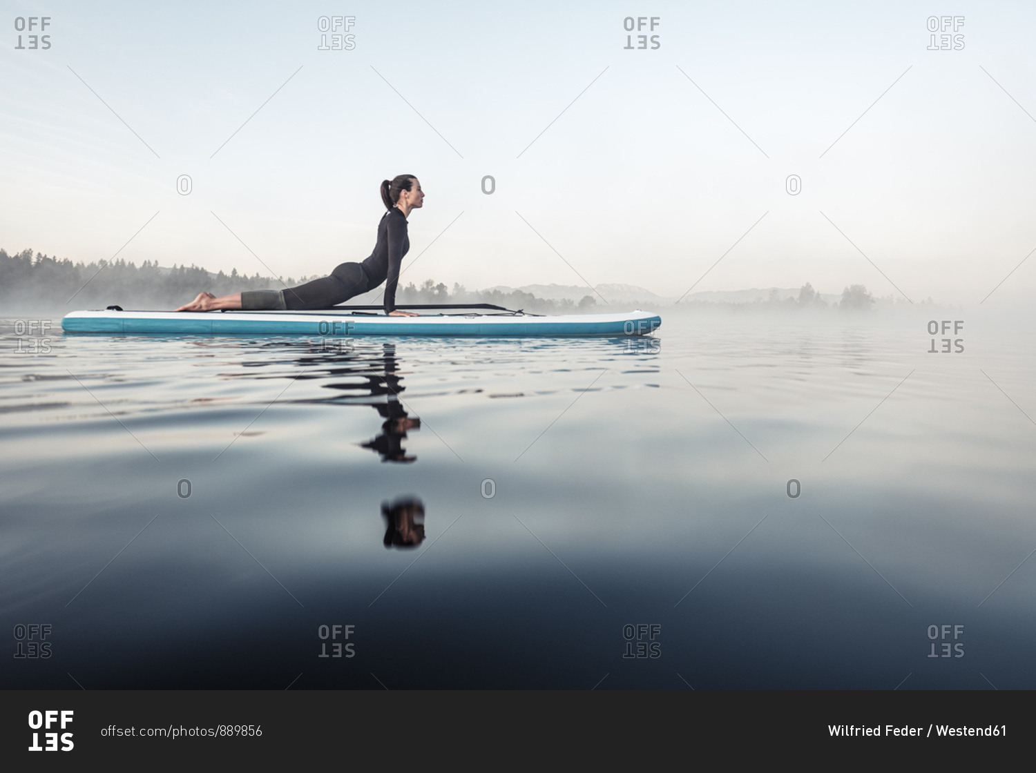Woman practicing paddle board yoga on lake Kirchsee in the morning- Bad Toelz- Bavaria- Germany