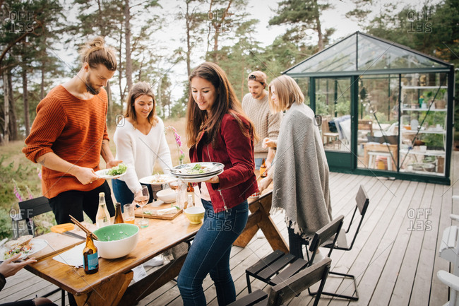 Male and female friends carrying leftover plates after dinner at patio