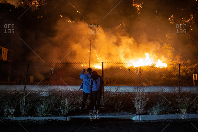 A couple evacuated from their home watch a wildfire burn near a highway in Los Angeles, CA