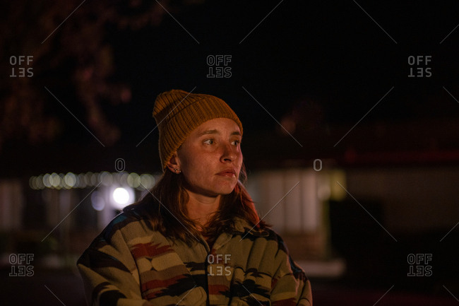A girl in a patterned vintage coat and beanie hat at a motel parking lot at night