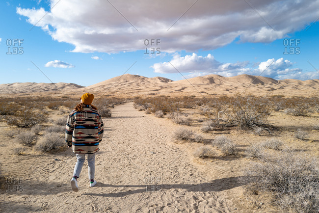 Young woman in Native American patterned jacket and mustard beanie explores Kelso sand dunes in California