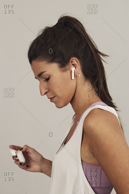 Side view of focused youthful sportswoman with earbuds listening to music on gray background in studio