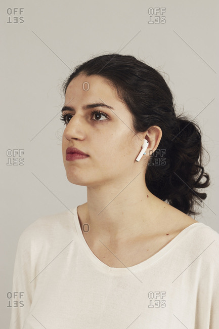 Side view of focused youthful sportswoman with earbuds listening to music on gray background in studio