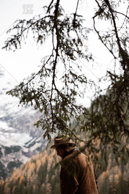 Back view of anonymous man traveler in casual wear standing with professional camera delighting in view of forest with Dolomites mountains on background at Italy