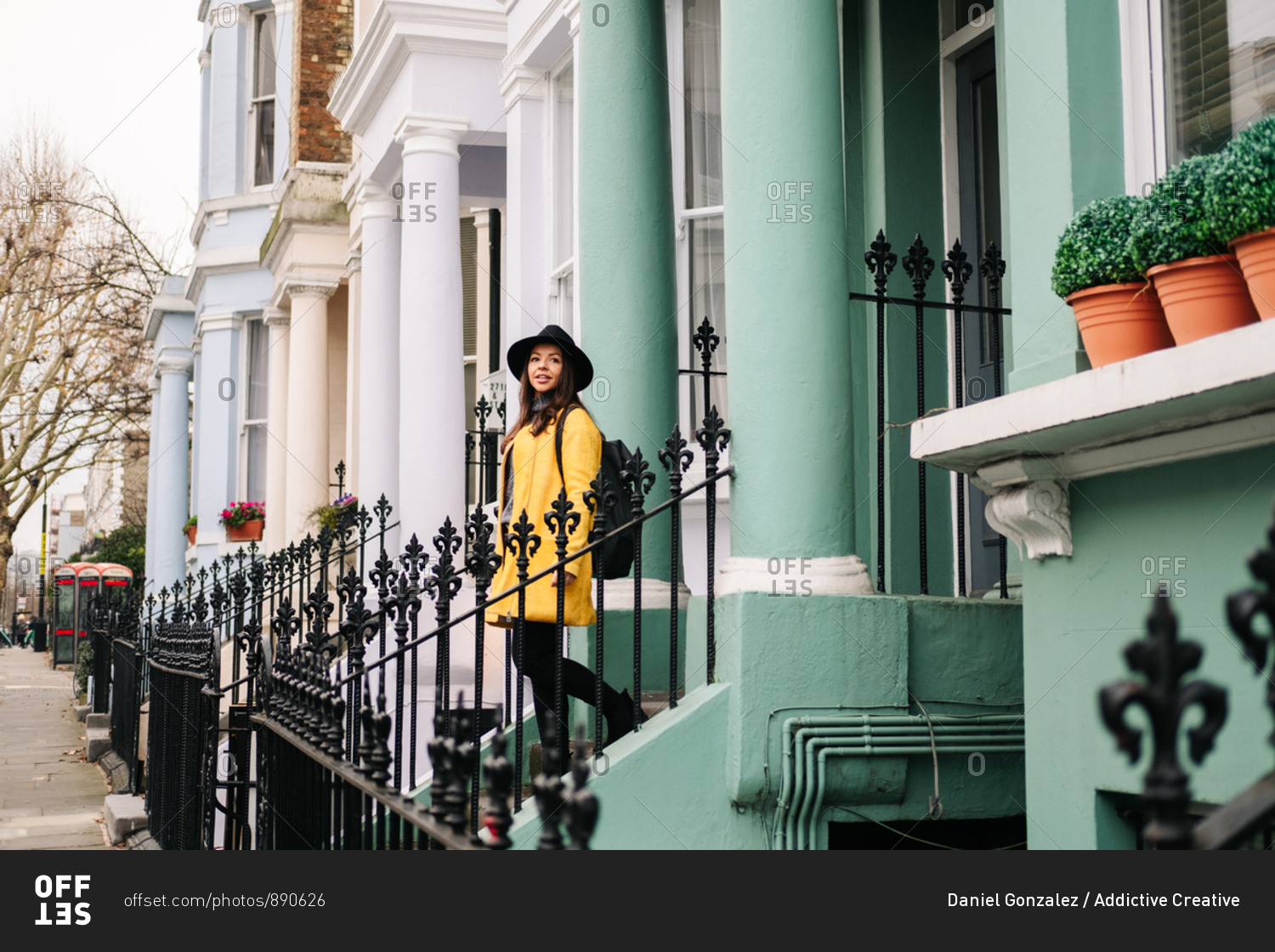 Happy stylish lady in yellow coat and hat smiling while standing in stairs in a house in the streets of London, United Kingdom