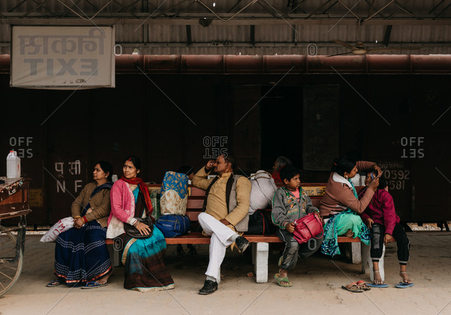 Praying Kumbh Mela Festival, Allahabad, India - February, 2018: Women in red and blue clothes festive man and kids waiting for transport sitting on station bench and looking away