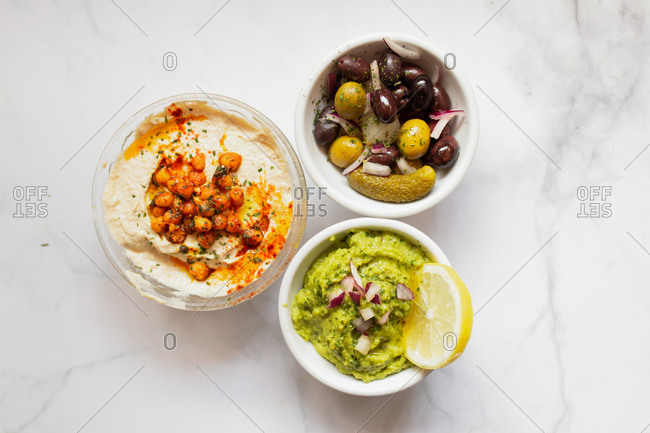 From above tasty healthy hummus green sauce cut onion salted cucumbers decorated with sliced lemon in white bowls on table
