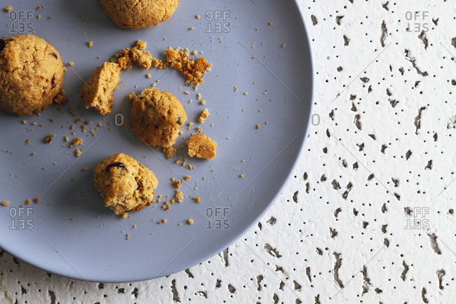 Fresh brown bitten cookies with chocolate crumbs lying on colorful ceramic plates on white spotted table against blurred white wall