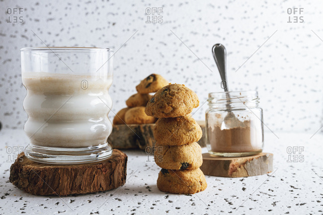 Tasty brown cookies on wooden coasters standing on sackcloth and transparent jar of cacao powder and glass of dairy beverage