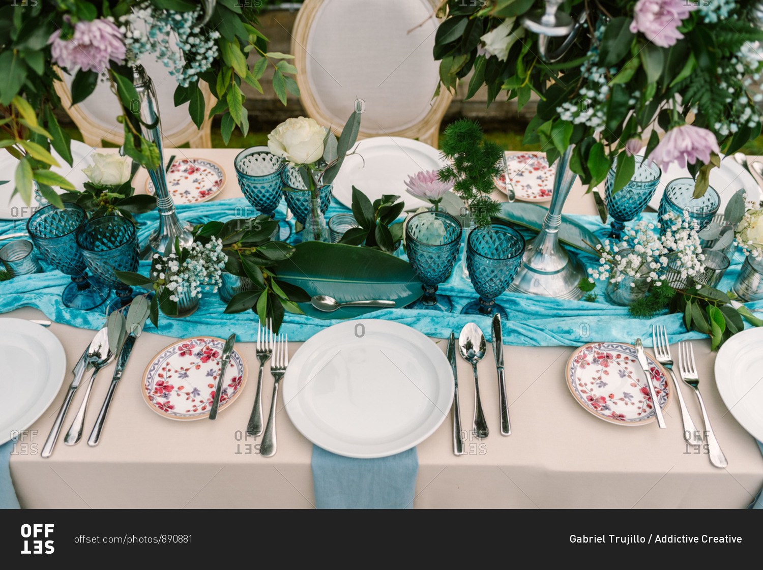 From above of wedding table decorated with blue and beige cloth and flowers bouquets in tall vases and served with porcelain plates and blue glasses