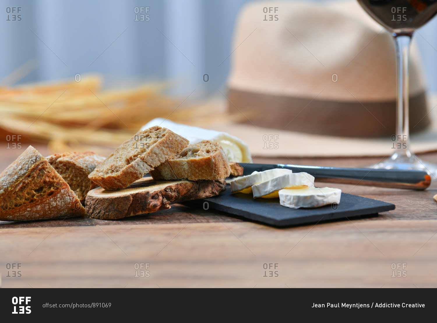 Tasty homemade slices of white cheese and fresh crusty bread with bottle and glass of red wine on rustic wooden table