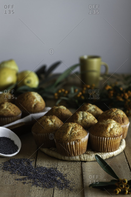 Appetizing fresh baked cupcakes on wicker stand on wooden table decorated with berries lemon and poppy seed for baking