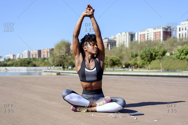 Young African American fitness female in sports top and leggings sitting in lotus  pose and stretching