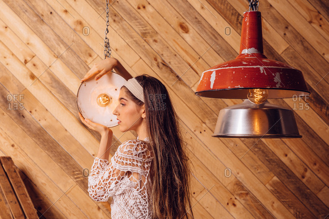 Young woman posing between ceiling lamps on wooden background