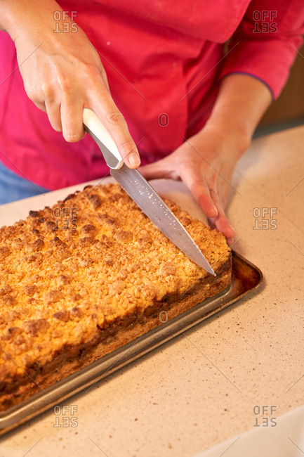 Crop anonymous woman in vivid pink clothes cutting with knife pie baked with tasty crust while standing at table and finishing cooking pastry at home