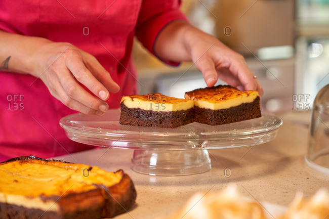 Crop anonymous woman in vivid pink clothes putting slices of pie baked with tasty crust on round glass stand at home