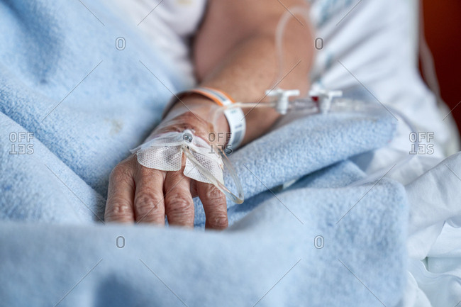 Unrecognizable mature person with cannula with remedy attached to arm lying on medical med during recovery in hospital