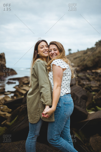 Relaxed women standing on stone on hill and hugging after walking in countryside on cloudy spring day and enjoying time together on cloudy spring day