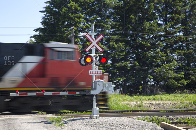 Train engine crossing rural crossing with barrier and lights on, Toronto, Ontario, Canada
