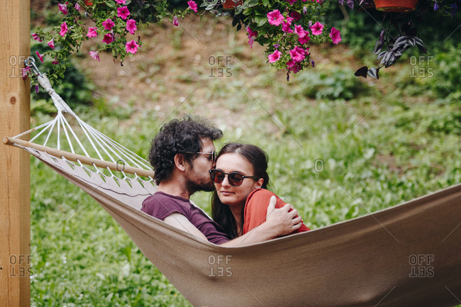 Young couple in love sharing a kiss outdoors in summer while resting in a hammock outdoors