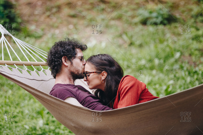 Young couple in love sharing a kiss outdoors in summer while resting in a hammock outdoors