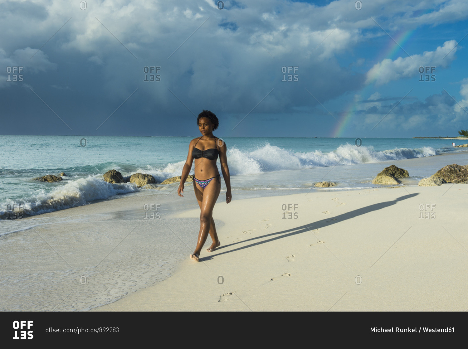 Woman wearing bikini walking at Grace Bay beach against cloudy sky- Providenciales- Turks And Caicos Islands