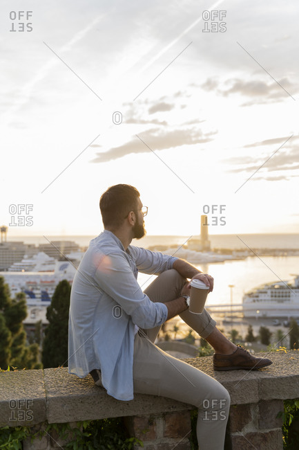 Man sitting on a wall on lookout above the city with view to the port- Barcelona- Spain