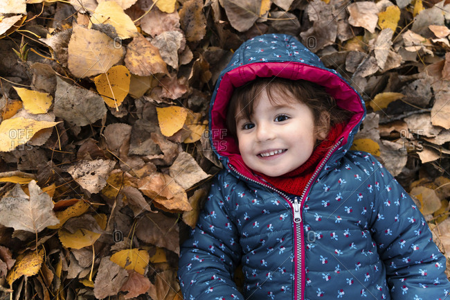 Portrait of happy little girl lying on autumn leaves