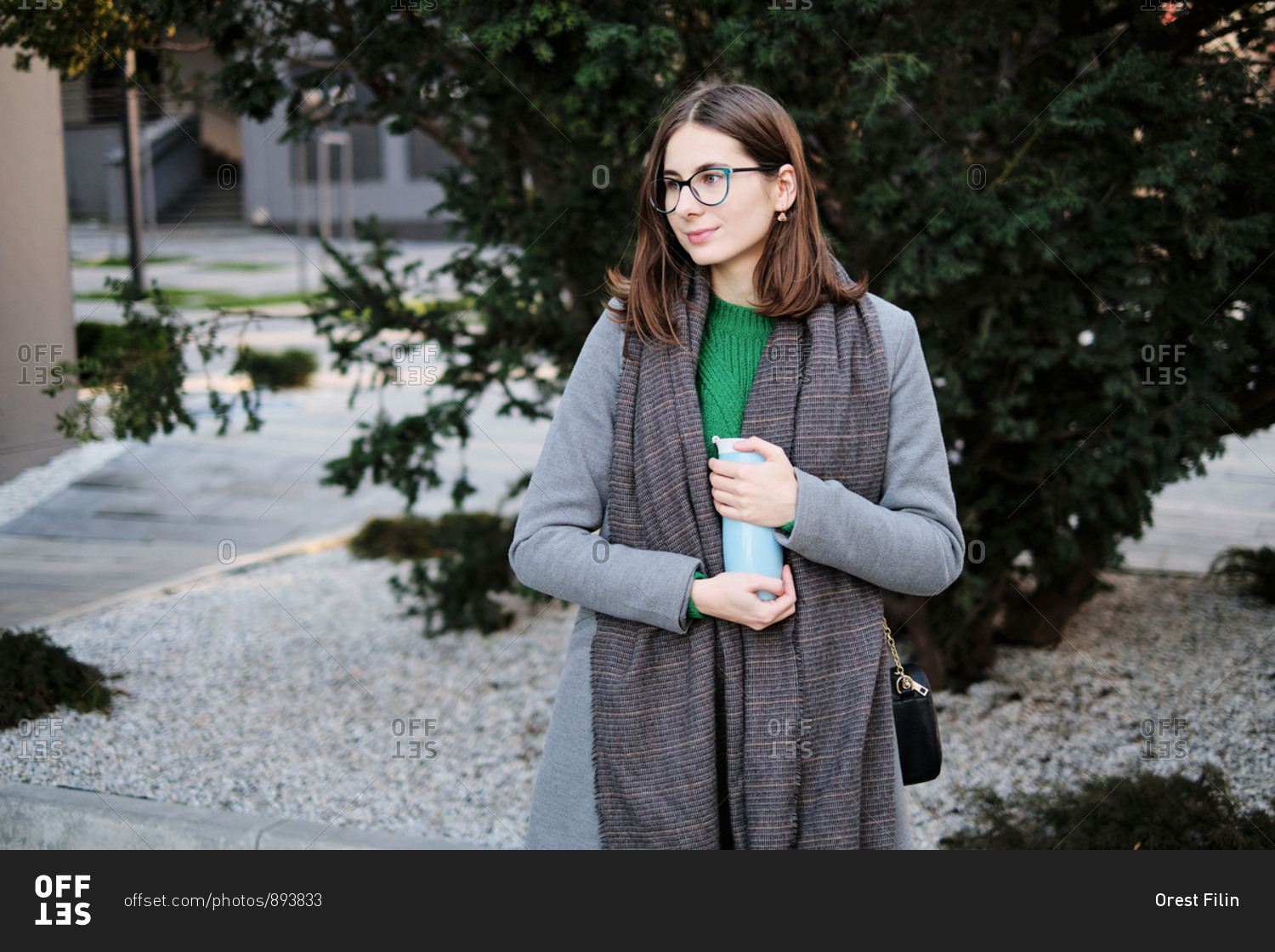Young woman wearing a grey coat in an urban location with vacuum flask in her hands