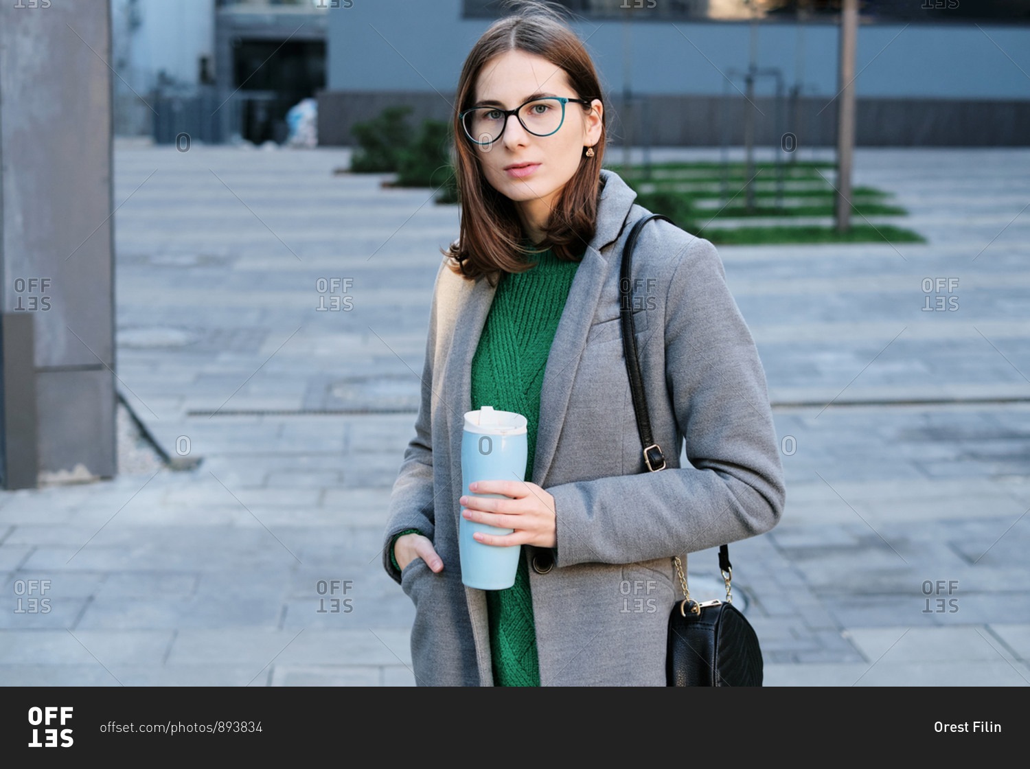 Attractive woman wearing a grey coat in an urban location with vacuum flask in her hands