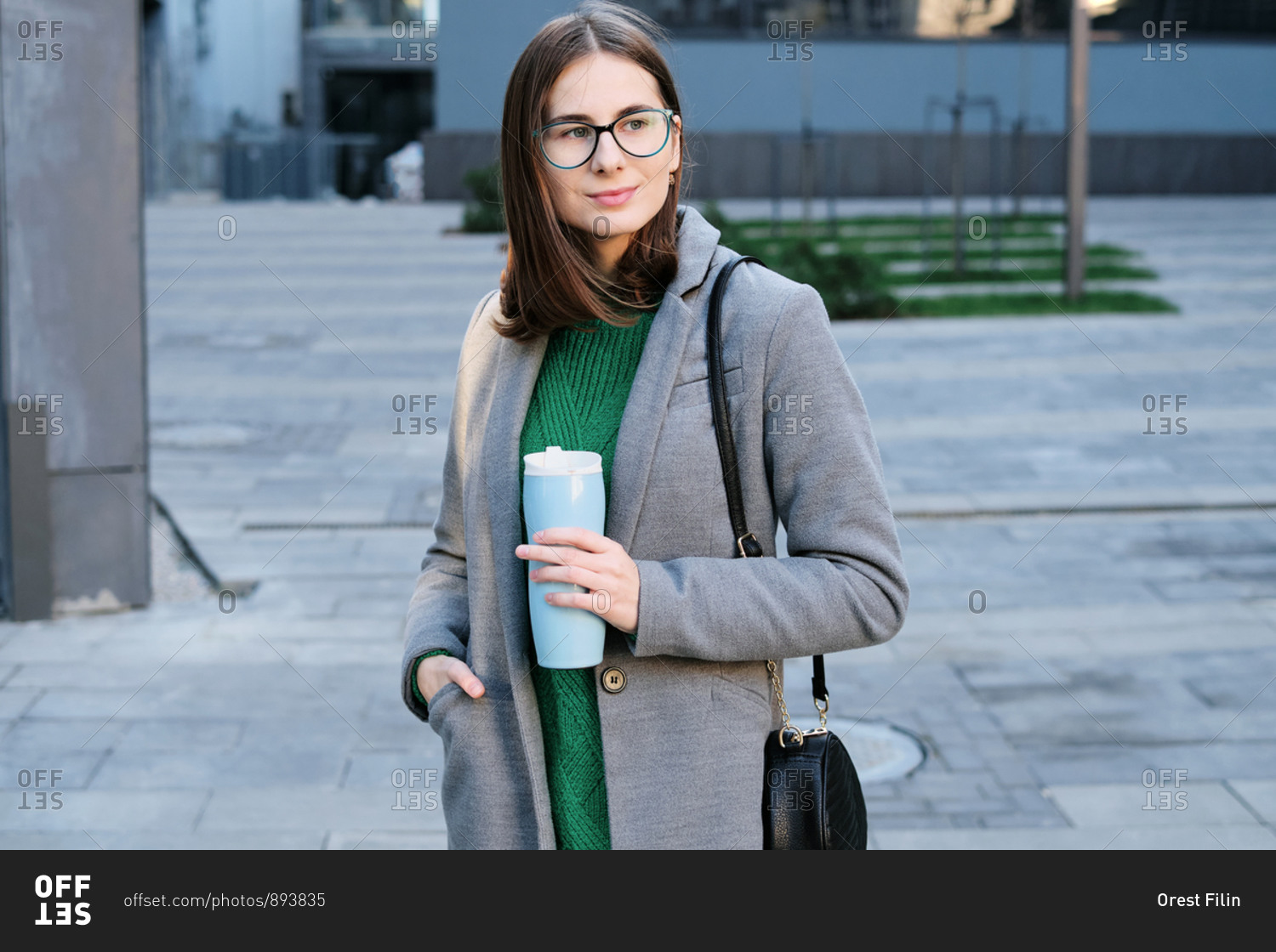 Attractive young woman wearing a grey coat in an urban location with vacuum flask in her hands