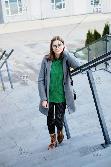 Young woman wearing a grey coat standing on steps of urban building