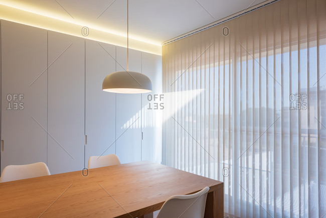 Table with chairs located under lamp near window in simple light conference room in modern office