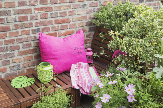 Balcony with bench- pink cushion- blanket- lanterns and various potted plants