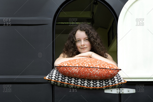 Portrait of young woman leaning on cushions looking out of caravan