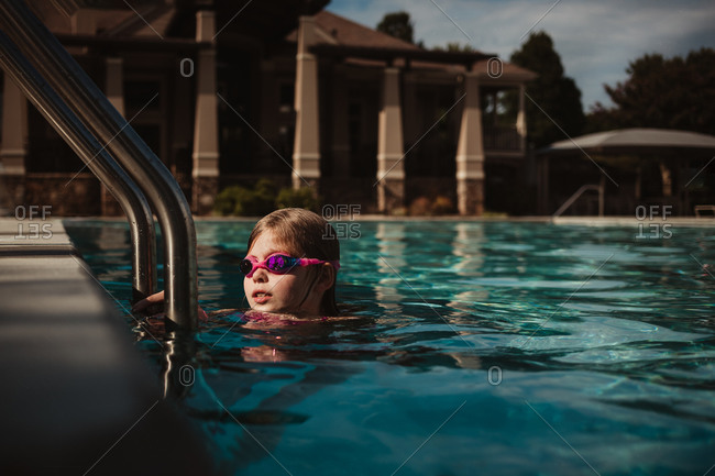 Little girl wearing goggles near ladder in a pool