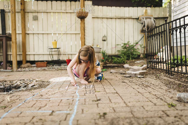 Little girl wearing arm cast draws on patio with sidewalk chalk