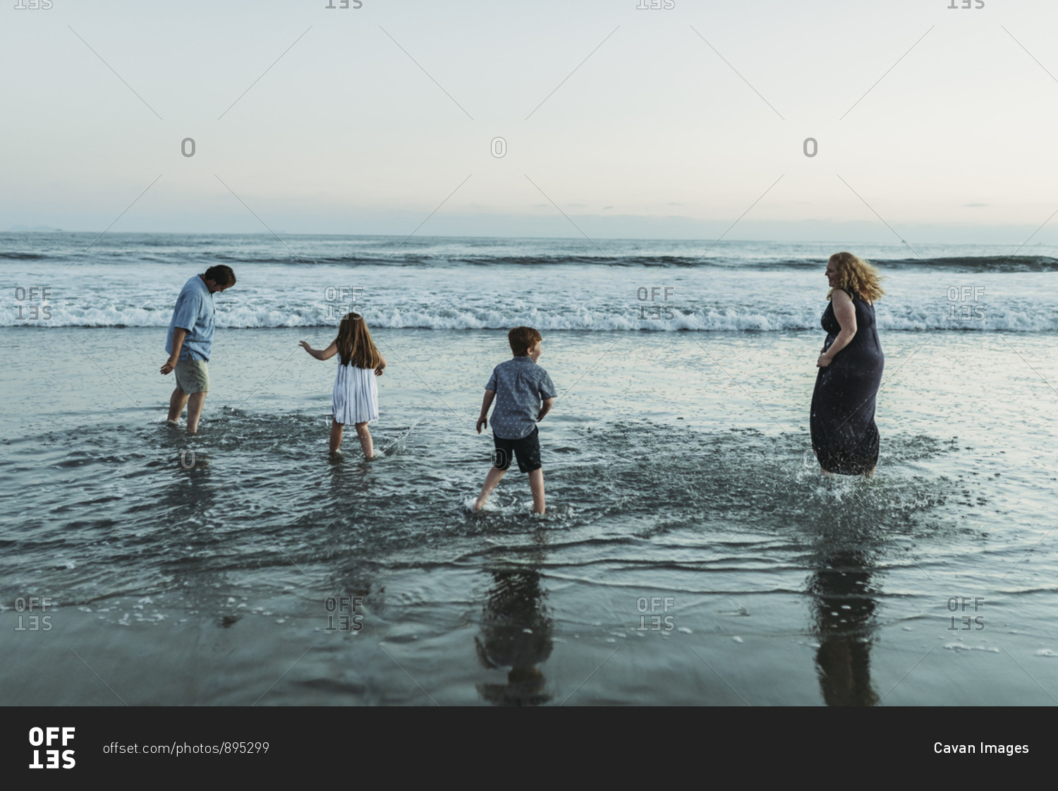 Family of four playing and splashing each other in ocean at dusk