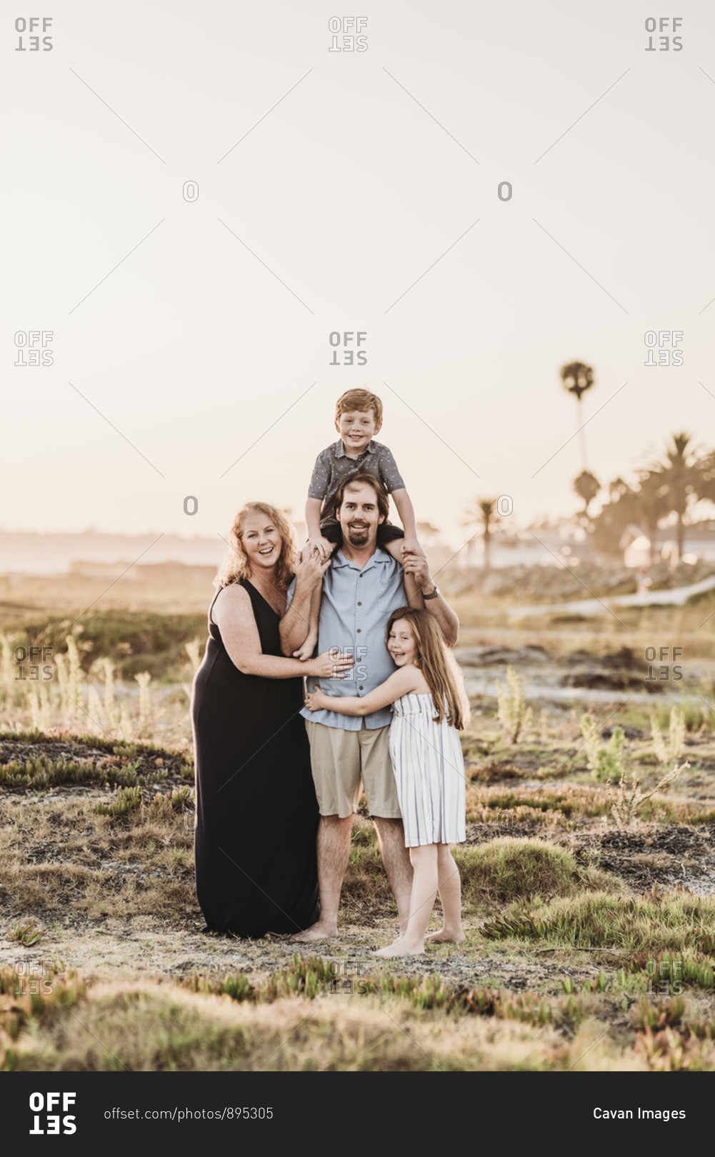 Portrait of happy smiling family of four hugging on beach at sunset