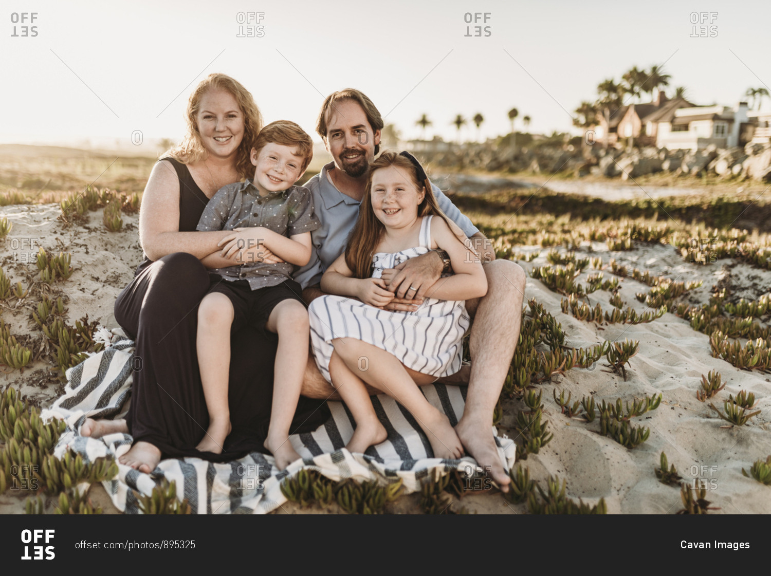 Portrait of family of four sitting on blanket at beach during sunset