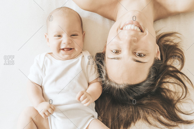 Mother and newborn son stretched out in bed laughing