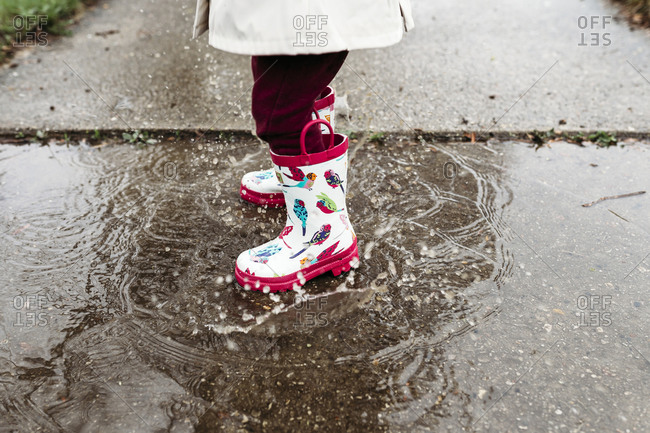 Low section of girl wearing rubber boots while standing in puddle